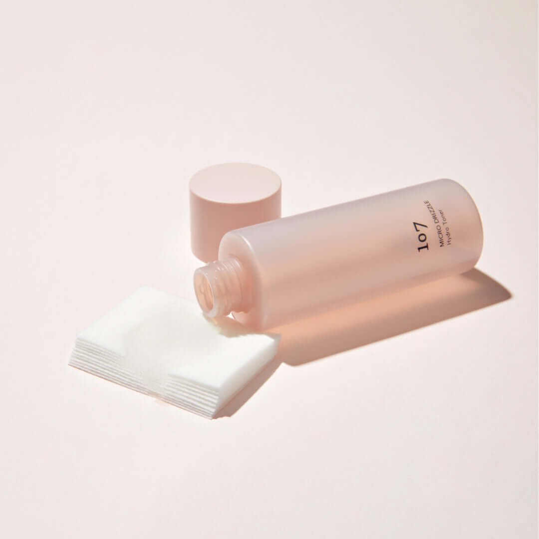 107 Micro Drizzle Hydro Toner 155ml bottle with open cap and cotton pads on a light background.
