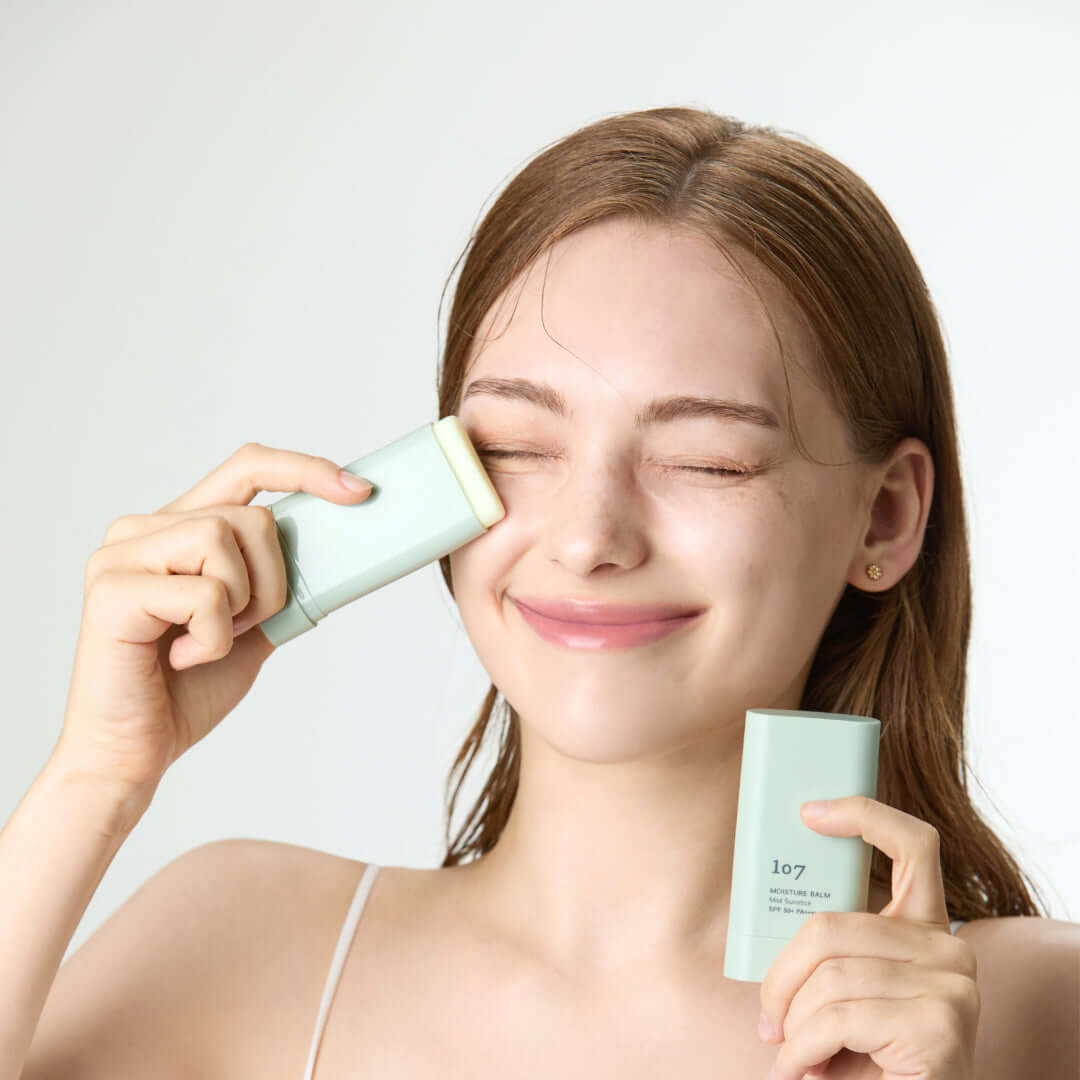 Woman applying 107 Moisture Balm Mild Sun Stick SPF50+PA++++ to her face, showcasing skincare routine with sunscreen protection.