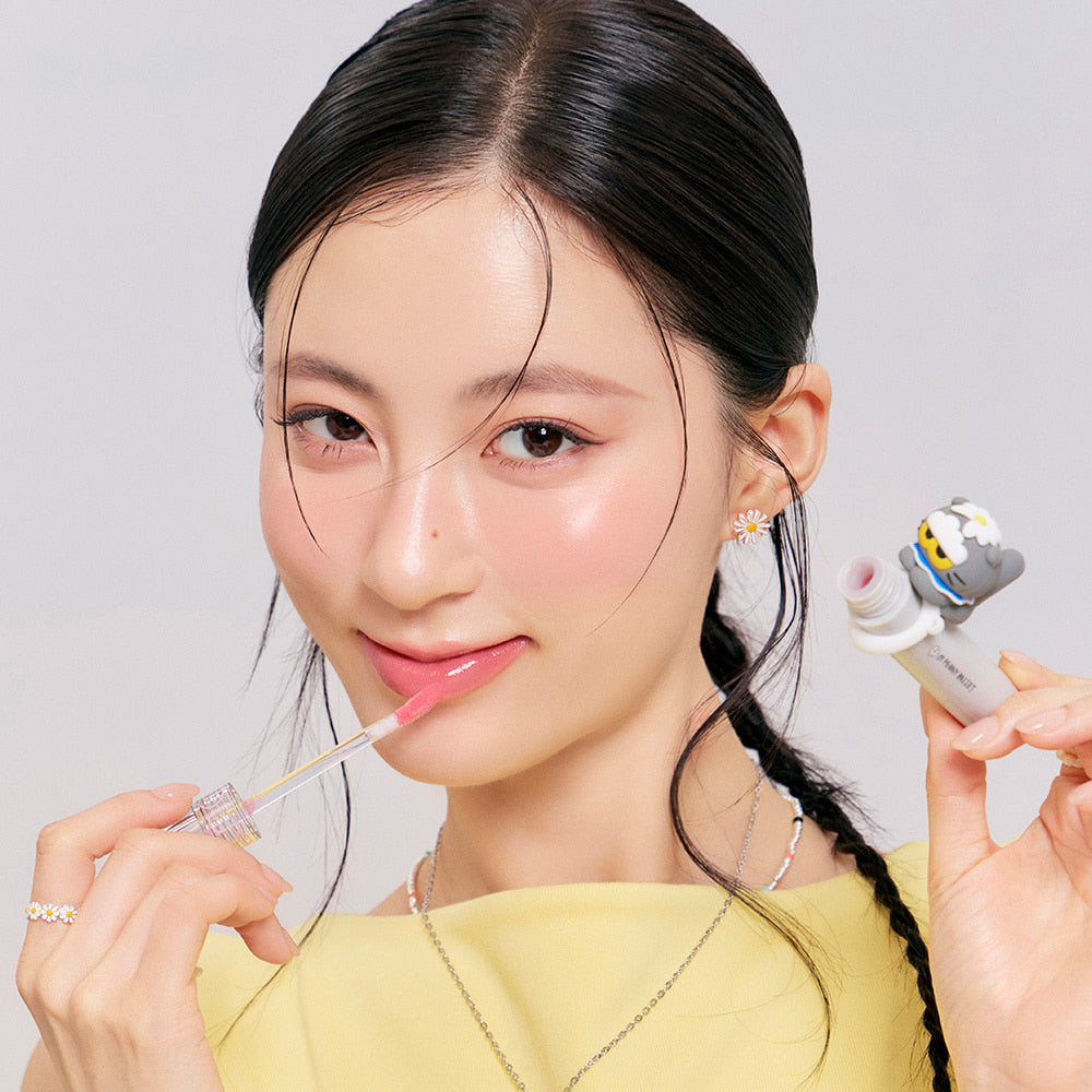 Woman applying ROMAND x Joanne Friends Glasting Color Gloss in a playful packaging with a smile, showcasing its glossy effect.