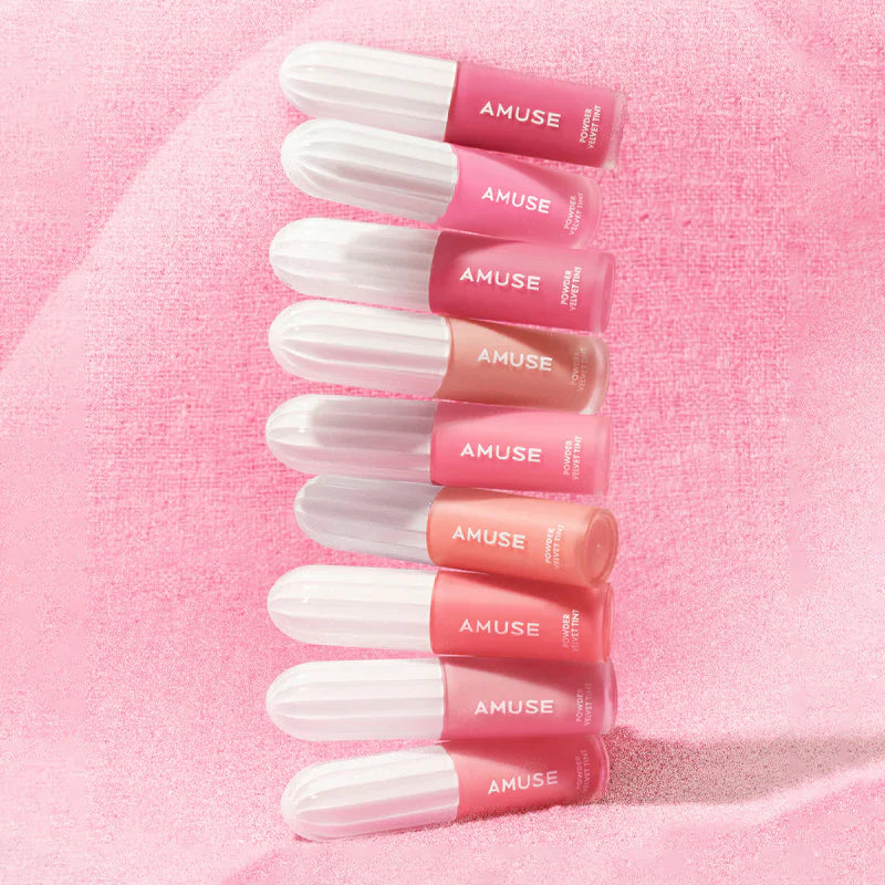Various shades of AMUSE Powder Velvet Tint lip products on a soft pink background.