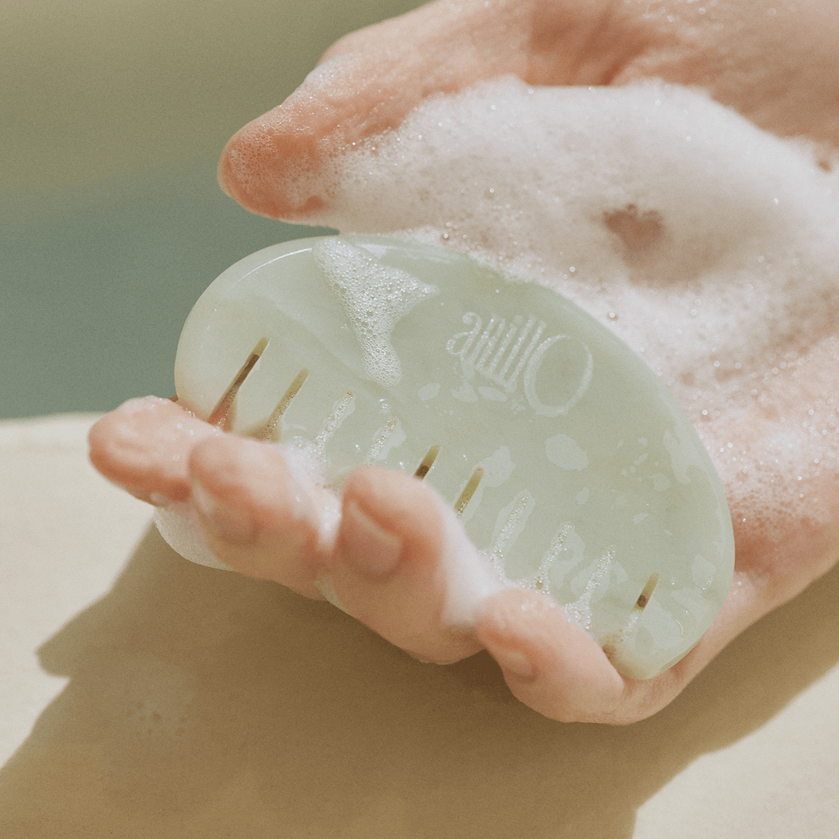 Hand holding a jade comb from ANILLO Special Scalp Care Set (Shampoo Bar & Jade GuaSha Comb), lathered with soap.