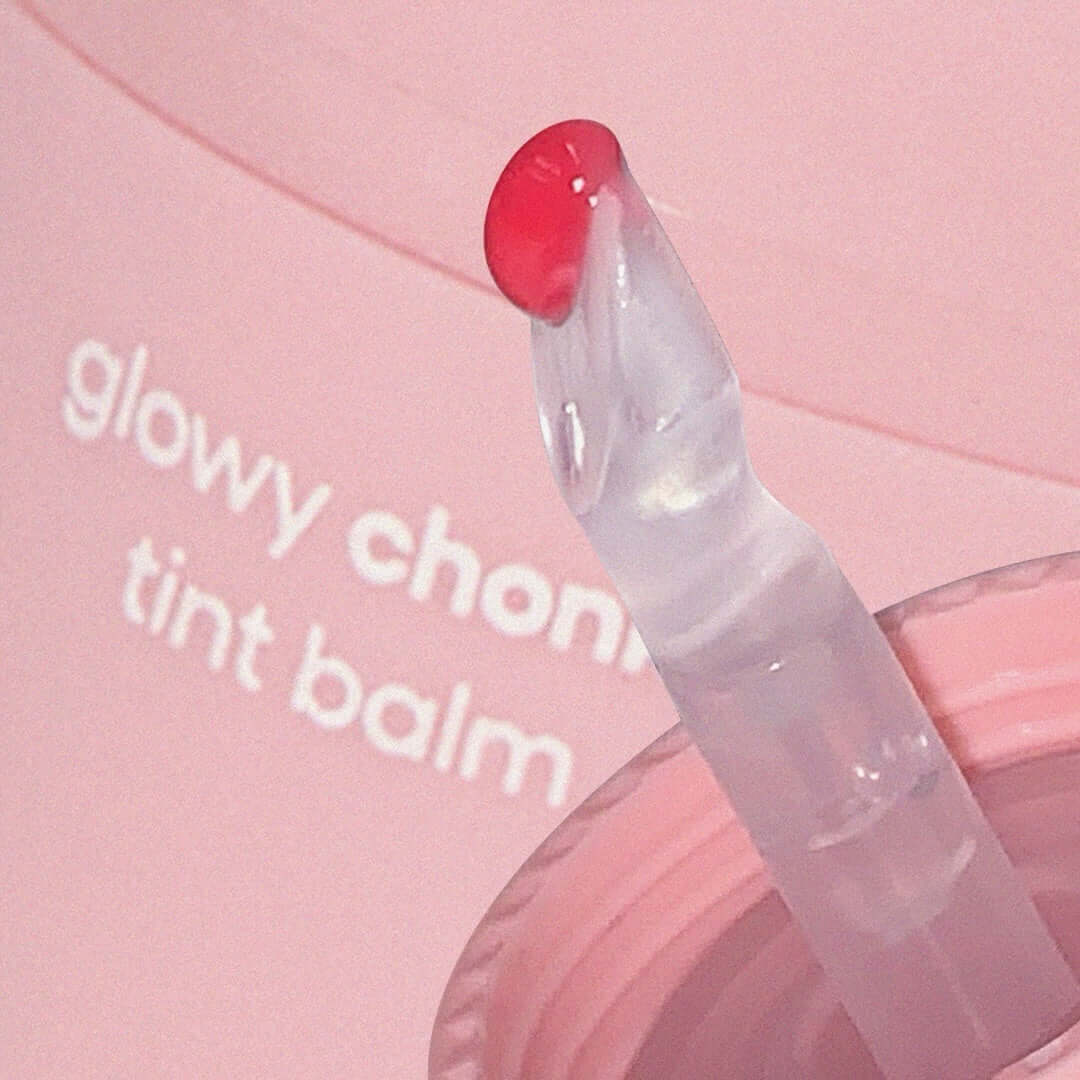 Close-up of AOU Glowy Chonky Tint Balm applicator with a tint of pink balm visible on a pink background.