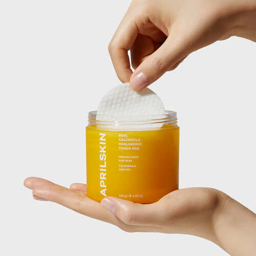 Hand holding APRILSKIN Calendula Hyaluronic Toner Pad with jar on white background, showcasing skincare product.