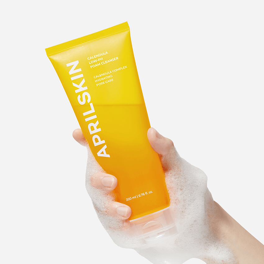 Hand holding a foamy tube of APRILSKIN Calendula Low PH Foam CLeanser with yellow packaging.