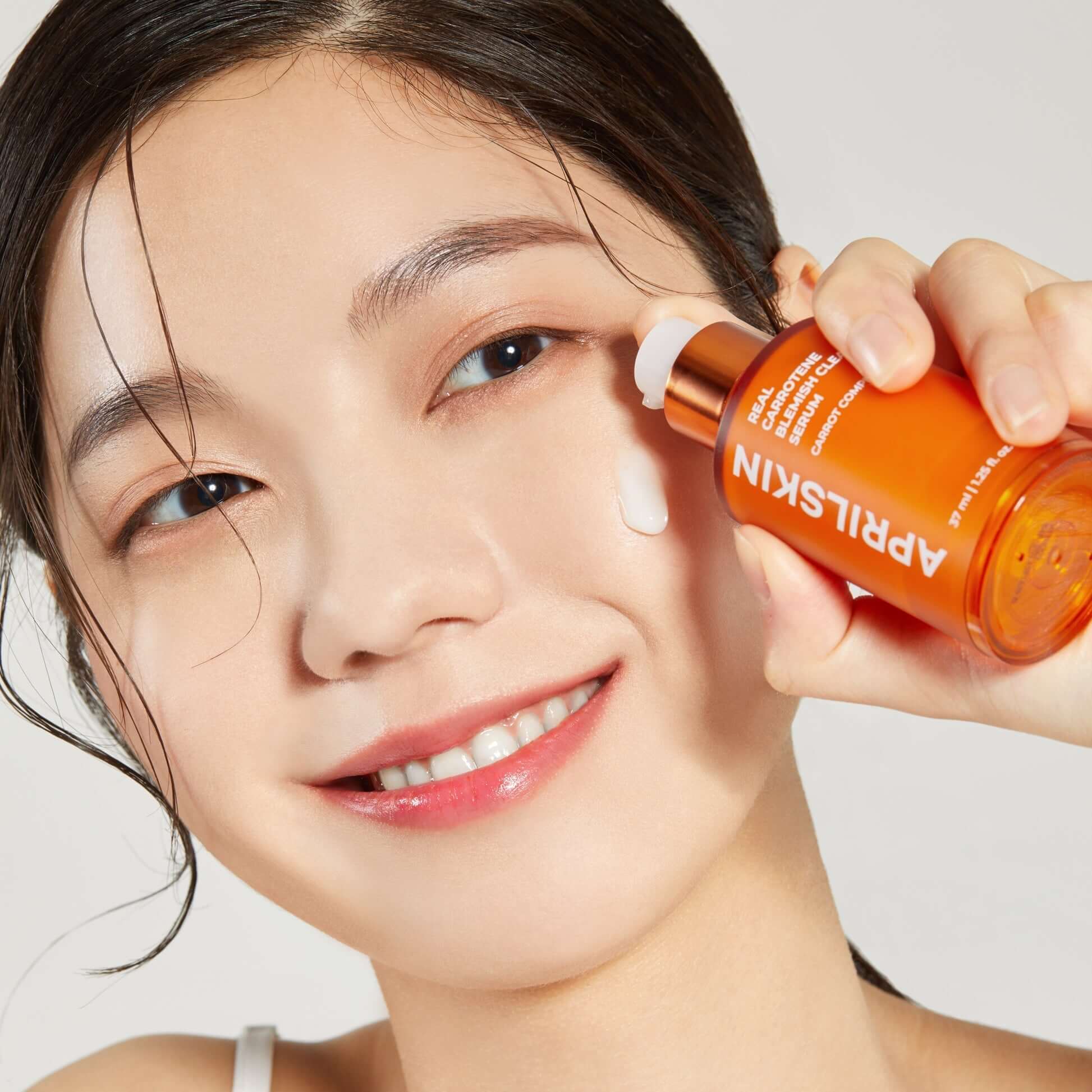 Model applying APRILSKIN Carrotene Clarifying Serum to face for skincare routine.