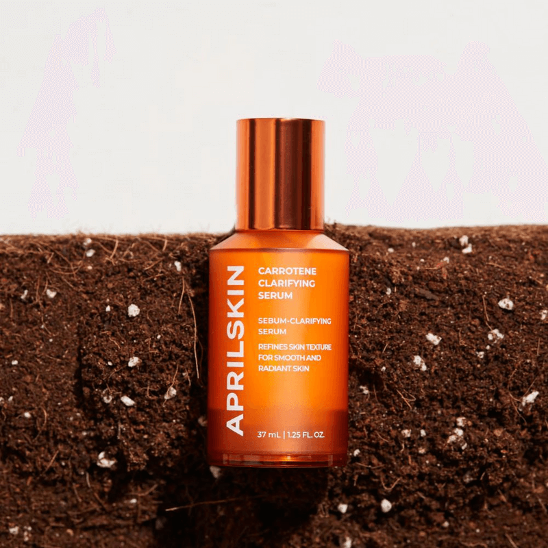 Orange bottle of APRILSKIN Carrotene Clarifying Serum on soil background for smooth and radiant skin.