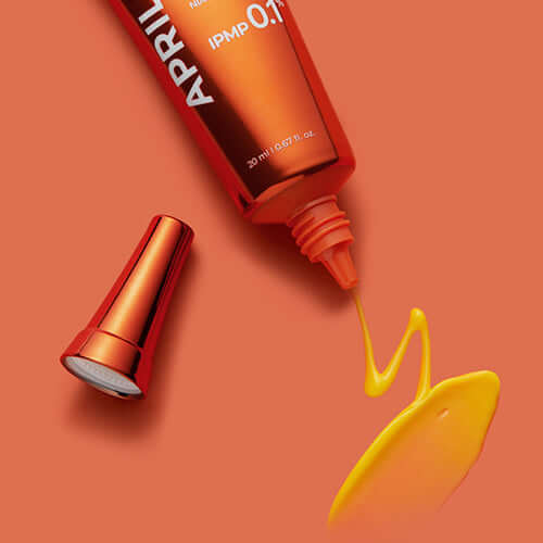 APRILSKIN Carrotene IPMP Clearing Solution tube with spilled product on orange background