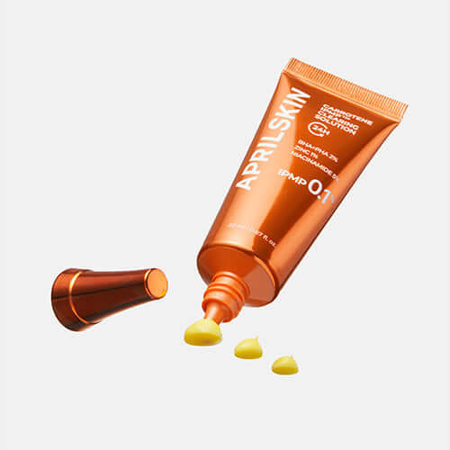 APRILSKIN Carrotene IPMP Clearing Solution in orange tube with open cap and product droplets.