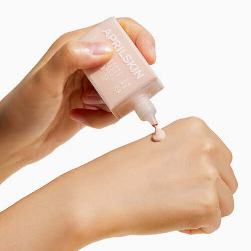 Hands applying APRILSKIN Tone-Up Skin Tint on skin for even tone and radiance.