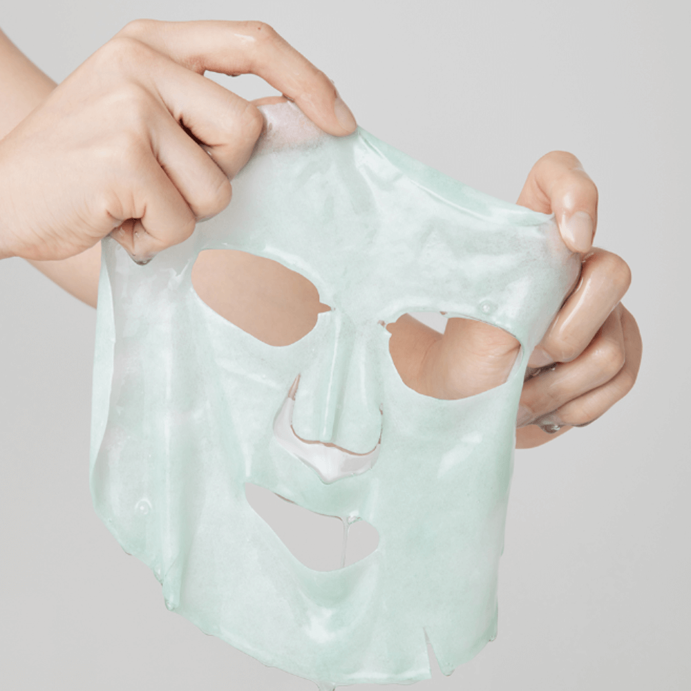 Hands holding a sheet from the ARENCIA Holy Hyssop Mask Pack (5 piece) against a plain background.