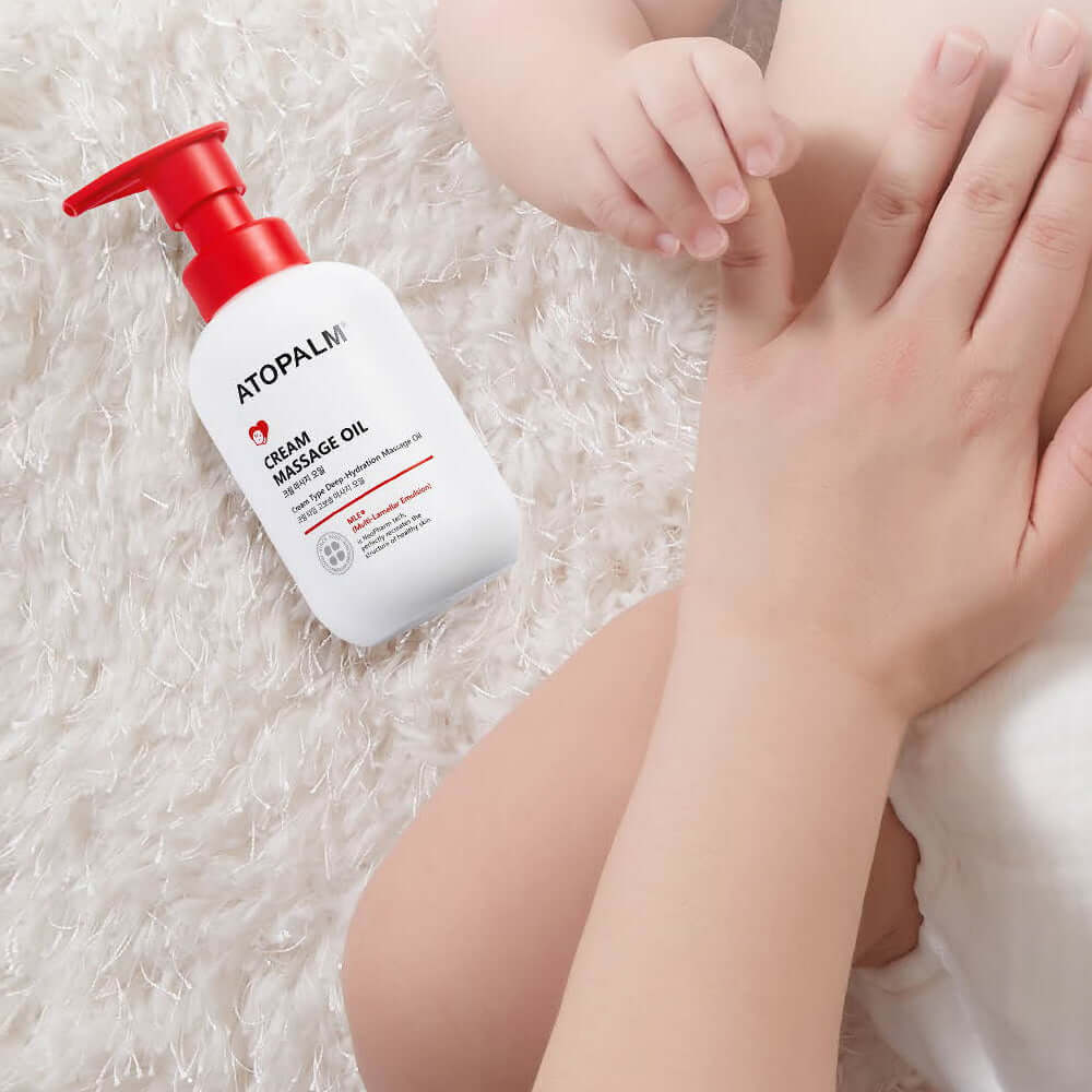 ATOPALM Cream Massage Oil 200ml bottle beside a baby's hand on a fluffy surface.