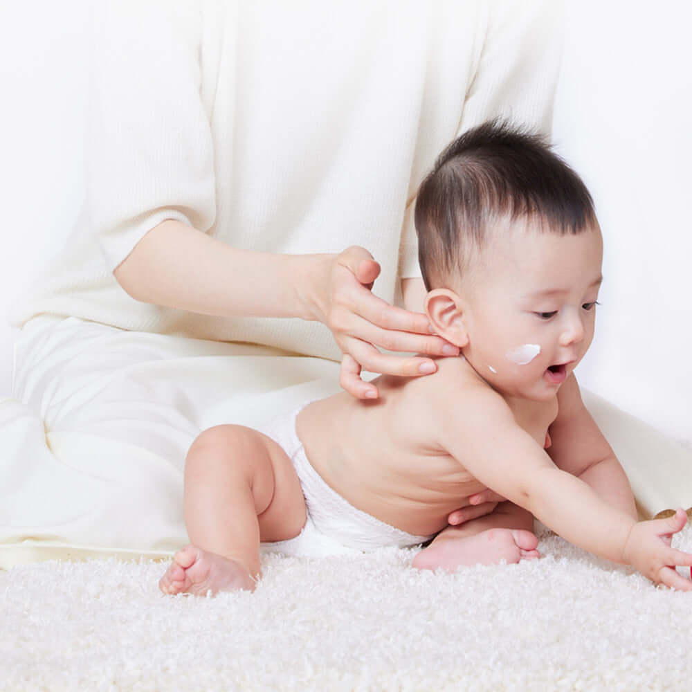 Baby with ATOPALM Panthenol Cream on face sitting with parent, showcasing moisturizing application.