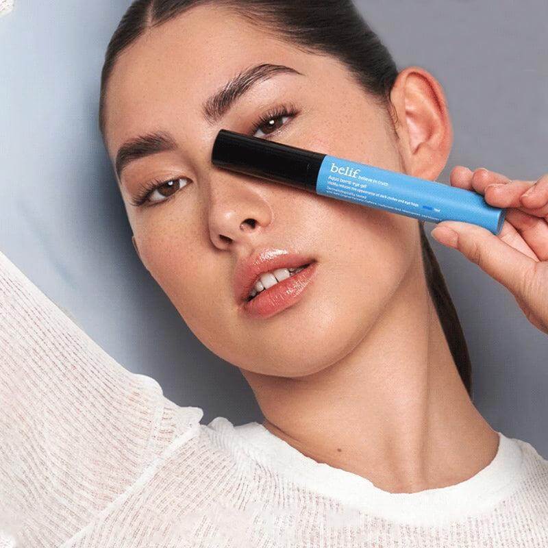 Model holding BELIF Aqua Bomb Eye Gel 15ml next to her face for skincare promotion.