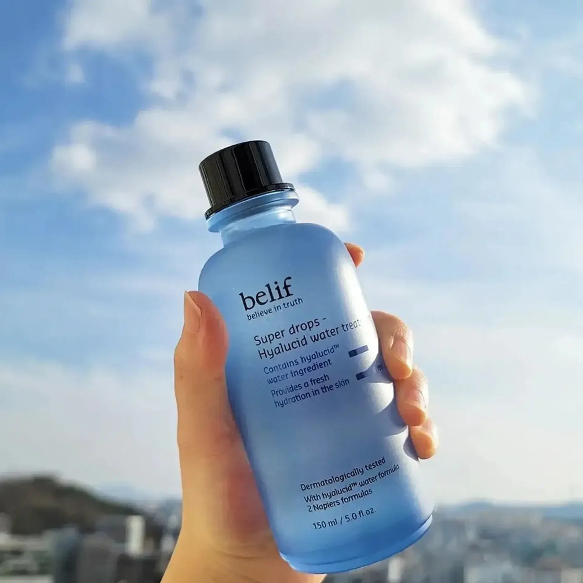 BELIF Super Drops-Hyalucid Water Treatment 150ml bottle held against a cloudy sky background