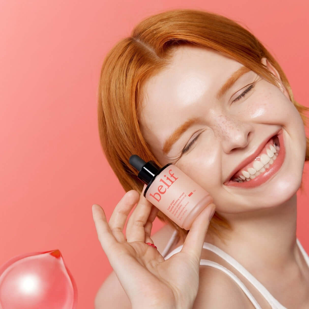 Smiling woman holding BELIF Super Drops Peptide Firming Serum 30ml against pink background.