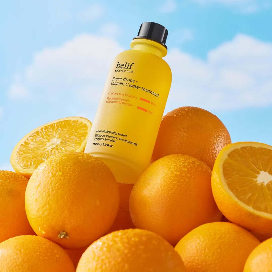 BELIF Super Drops-Vitamin C Water Treatment 150ml bottle surrounded by fresh oranges against a blue sky background