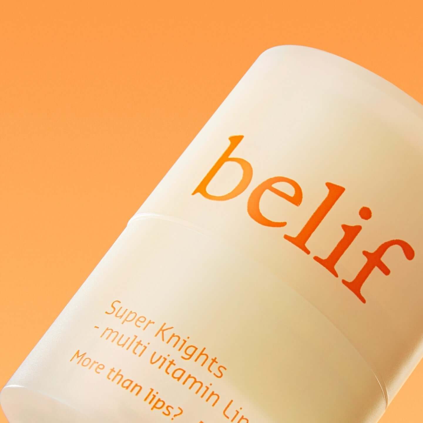 Close-up of BELIF Super Knight Multi Vitamin Lipcerin bottle against an orange background