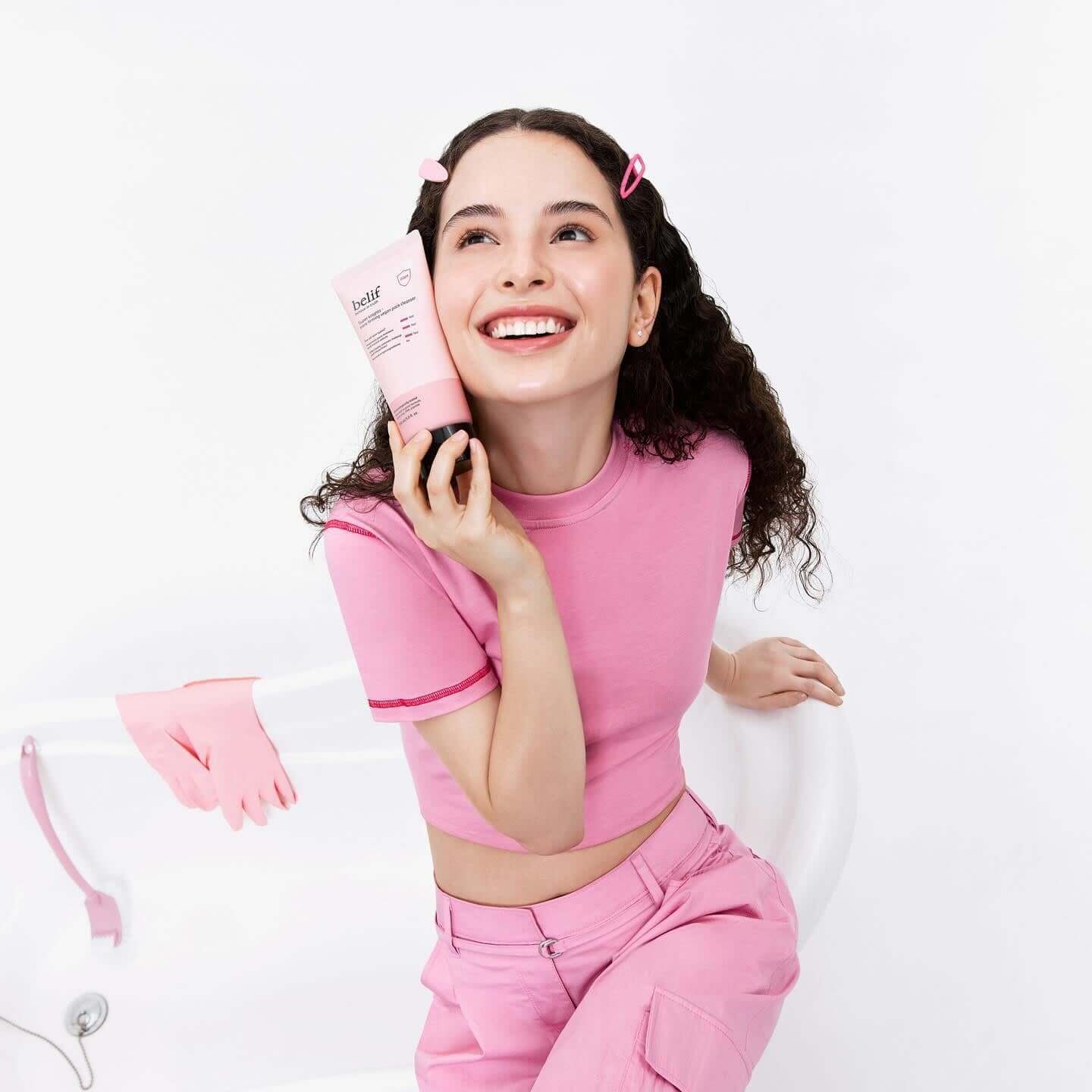 Smiling woman holding BELIF Super Knights Pore Fiming Vegan Pack Cleanser 150ml in a pink outfit.