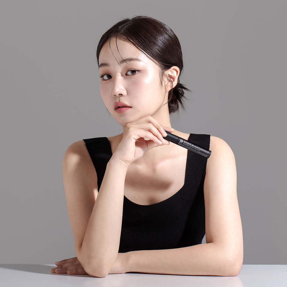 Woman holding BENTON Ernest Black Eyelash Nutrient 8ml against a gray background