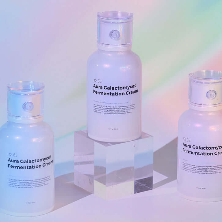 BLESSED MOON Aura Galactomyces Fermented Cream 50ml bottles displayed on a clear pedestal with pastel background
