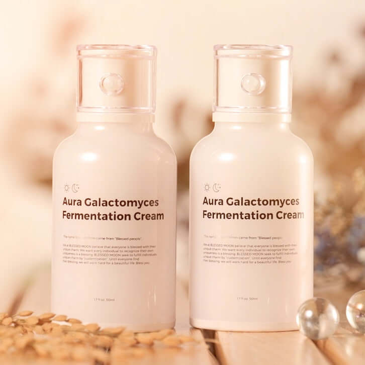 Photo of two bottles of BLESSED MOON Aura Galactomyces Fermented Cream 50ml on a wooden surface.