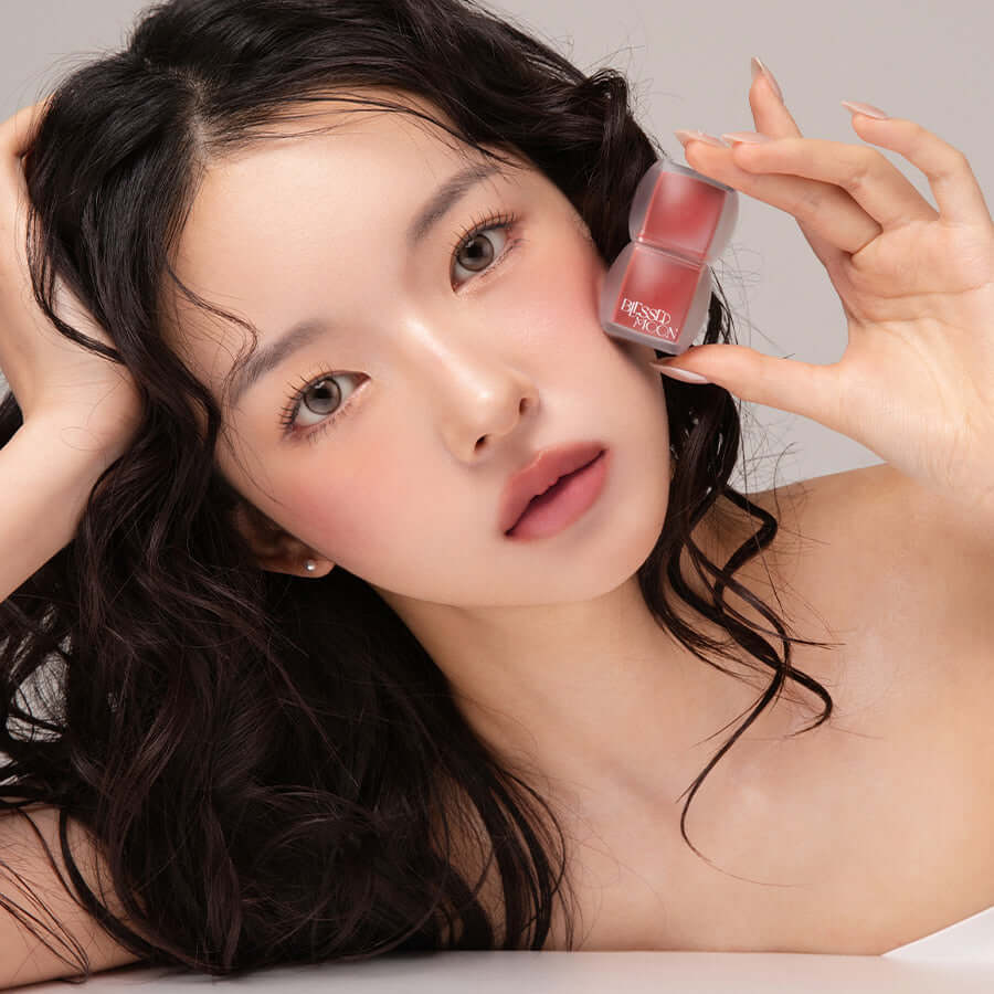 Model holding BLESSED MOON Veil Blur Lip Tint close to face showcasing lip color and product packaging.