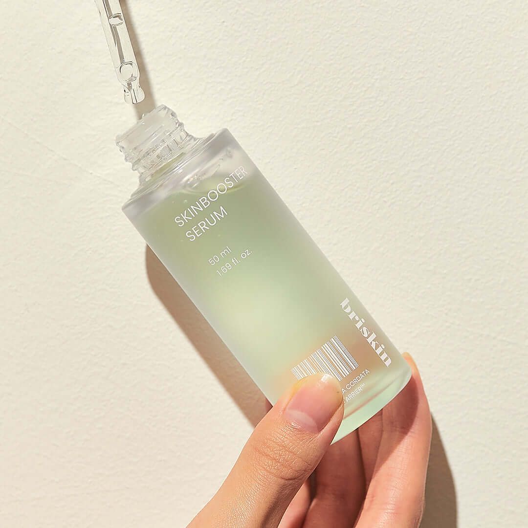 Hand holding BRISKIN Houttuynia Cordata Exo-Barrier Skinbooster Serum 50ml bottle against a light background