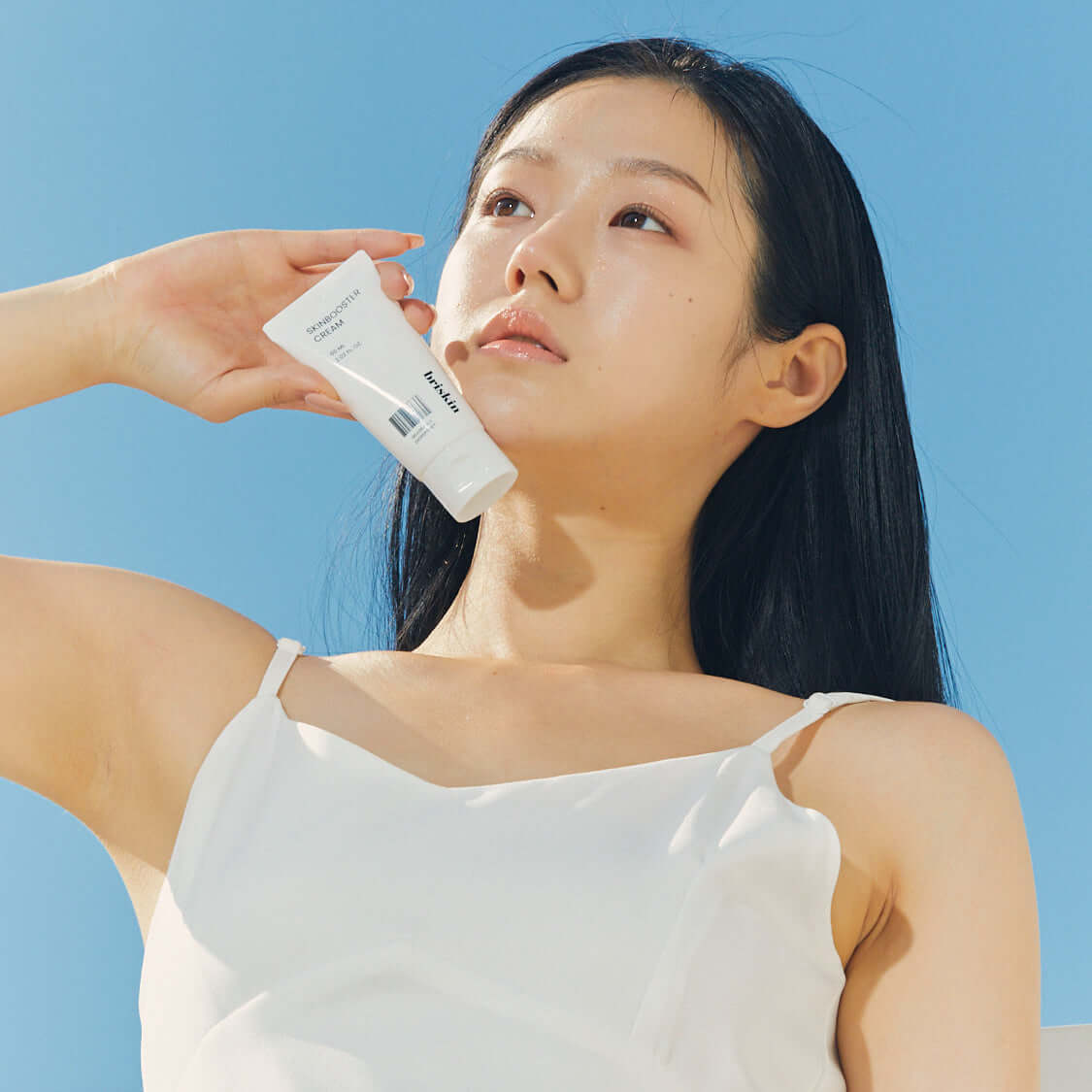 Woman holding BRISKIN Selaginella Exopeptide Skin Booster Cream 60ml against blue sky