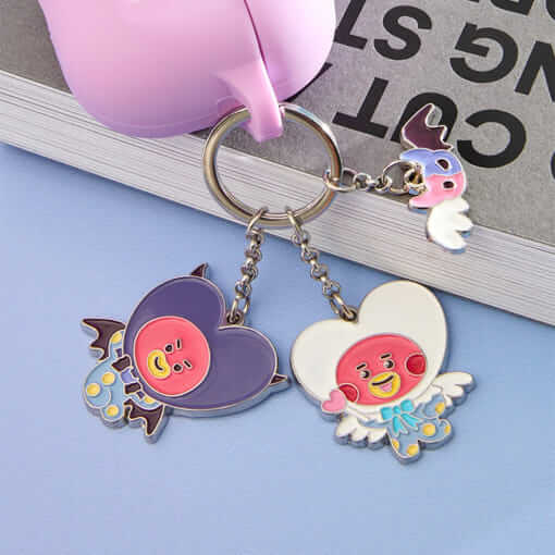 BT21 Angel & Villain Metal Key Ring featuring cute character designs on a table beside a pink cup.