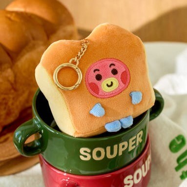 BT21 Bakery Plushy Keyring resting on a green soup mug with bread in the background.