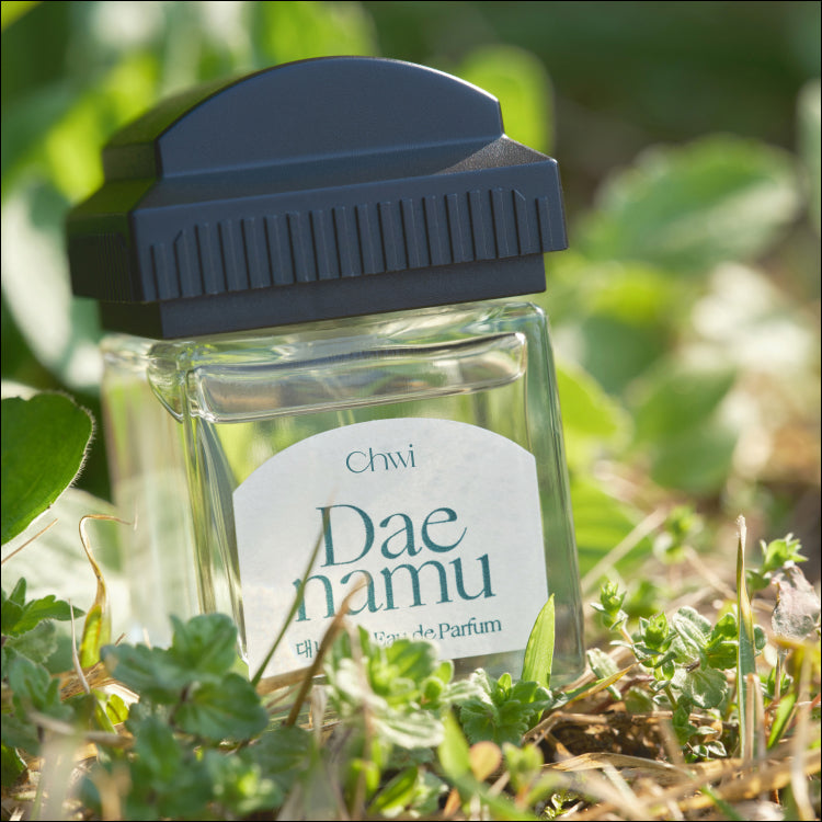 Bottle of CHWI (CHI) Eau De Parfume 50ml displayed outdoors on greenery.
