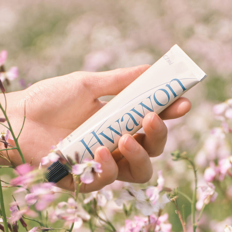 Hand holding CHWI (CHI) Hwa Won Hand Cream 50ml amidst flowers