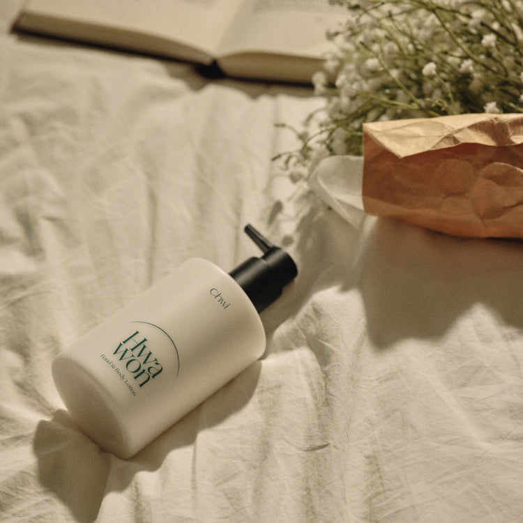 CHWI (CHI) Hwa Won Hand & Body Lotion 300ml on a bed with flowers and an open book nearby.