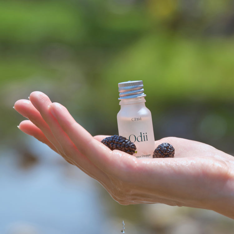 Hand holding CHWI (CHI) Odii Frangrance Dropper 10ml with natural scenery in the background.