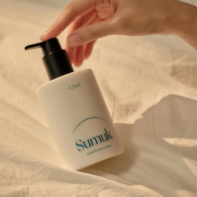 CHWI (CHI) Sumuk Hand & Body Lotion 300ml on a bed with hand reaching for pump bottle