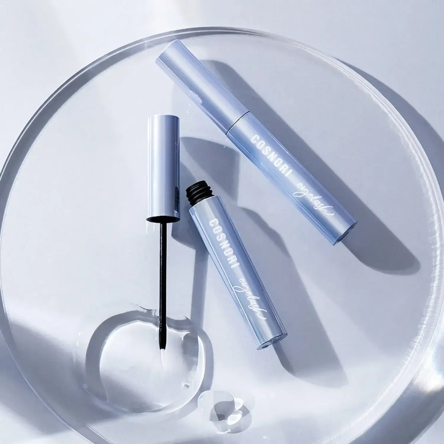 COSNORI Intensive Eyelash Serum on a clear tray with applicator brush.