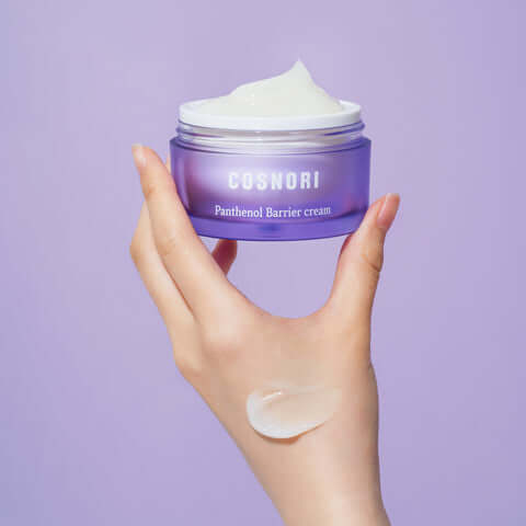 Hand holding open COSNORI Panthenol Barrier Cream 50ml against purple background