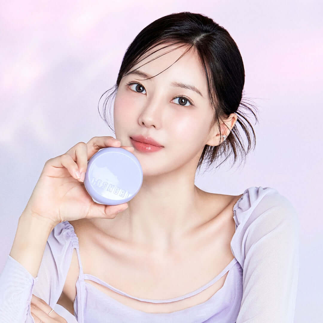 Woman holding a COSNORI Panthenol Barrier Cushion SPF50+PA++++ in a soft-lit setting. Enhance your skincare routine with this cushion.
