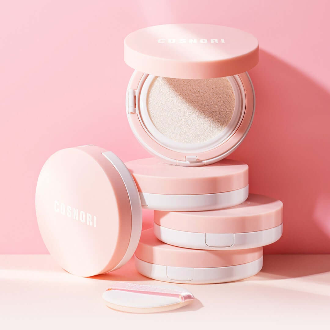 COSNORI Tone-up Cream Cushion in pink packaging, open with a sponge applicator next to it on a pastel pink background.