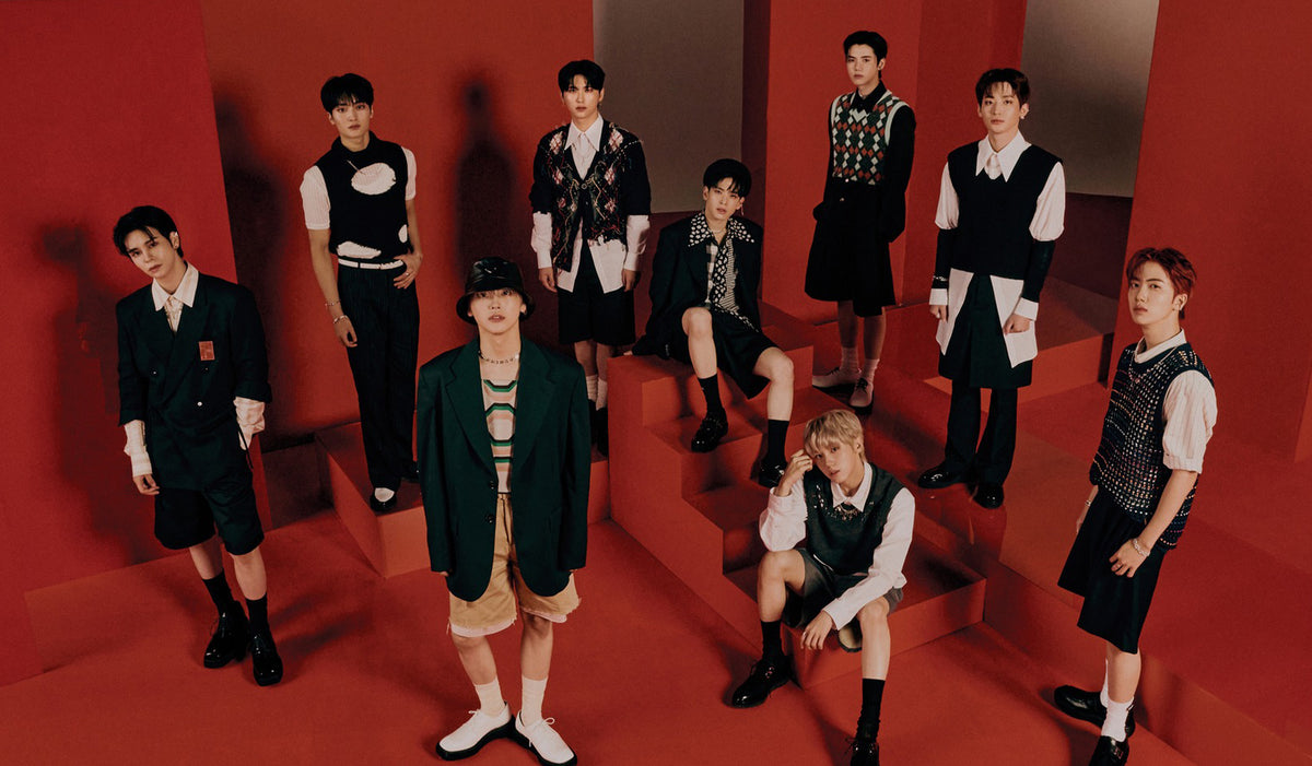 Nine individuals in fashionable outfits pose on a geometric red set, showcasing modern style.