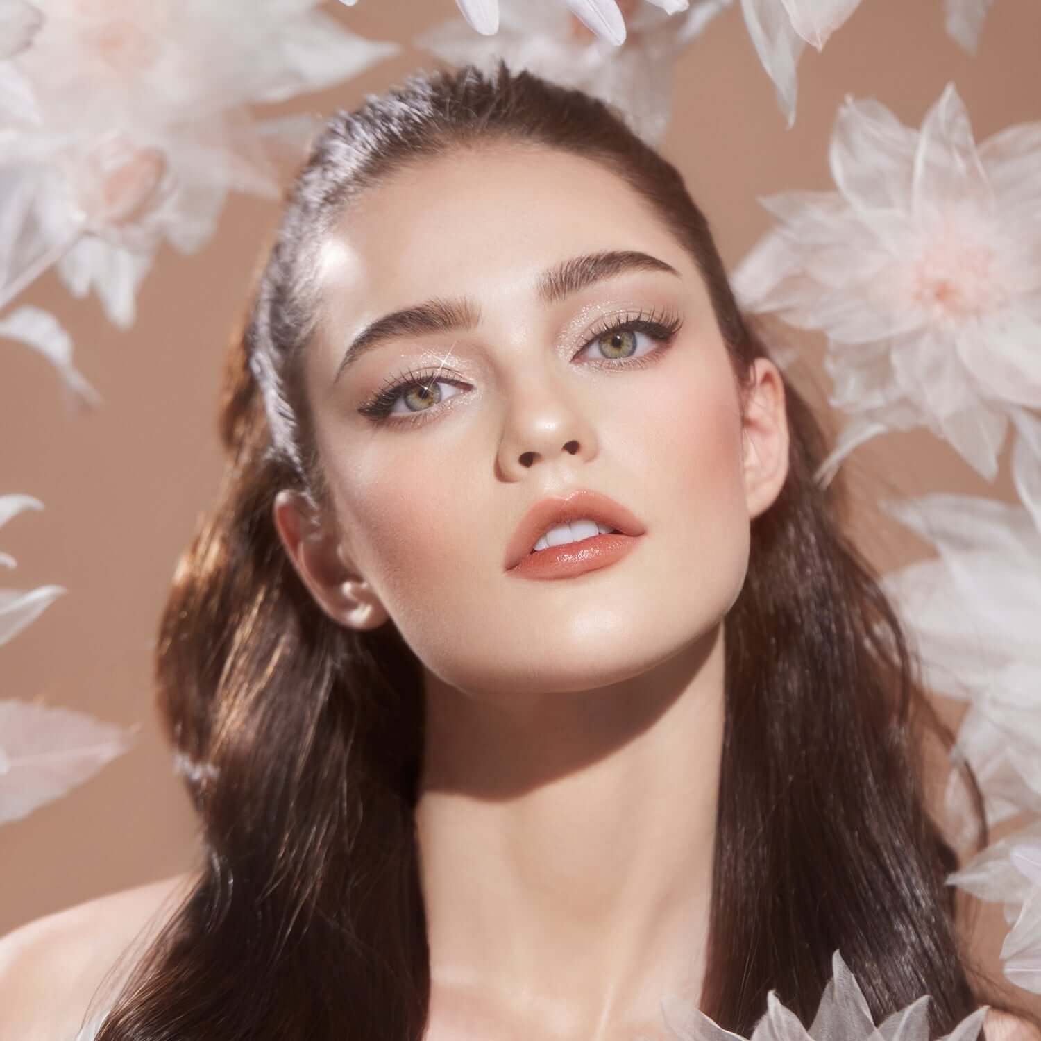Model wearing DEAR DAHLIA Blooming Edition Endless Glow Illuminator surrounded by flowers, showcasing radiant skin and natural makeup look.
