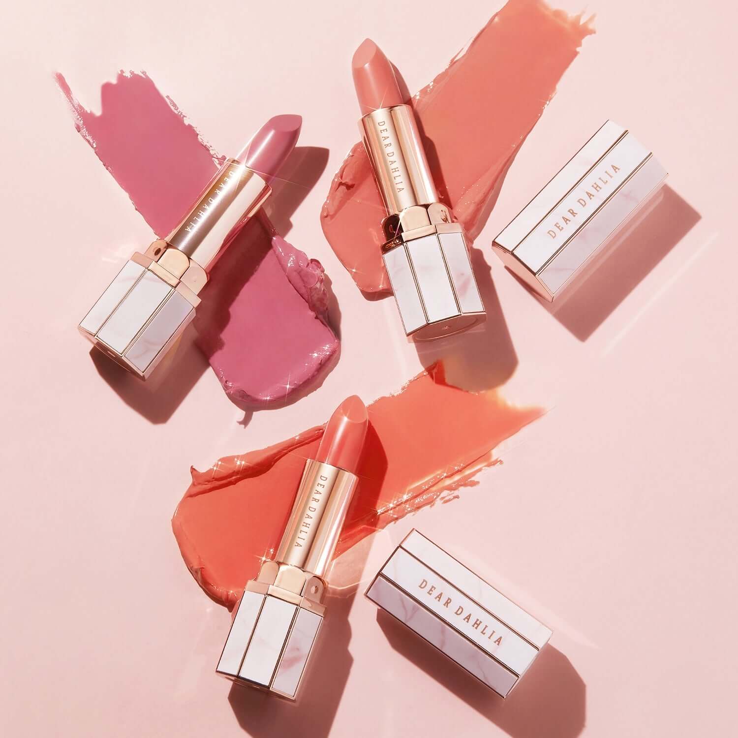 DEAR DAHLIA Blooming Edition Lip Paradise Sheer Dew Tinted Lipstick in assorted shades on a pink background.