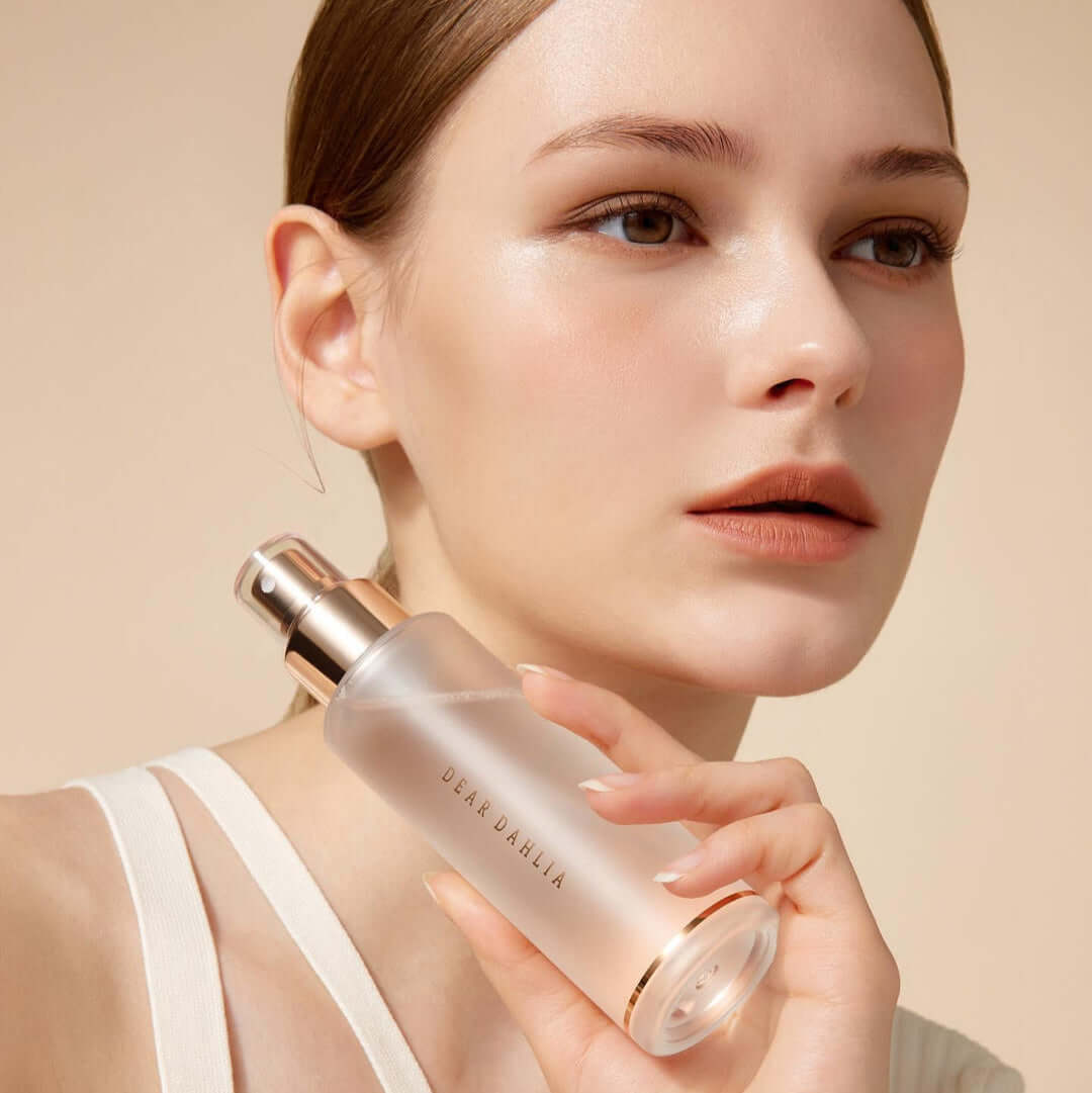 Woman holding DEAR DAHLIA Endless SKin Setting Spray bottle close to her face in a neutral background.