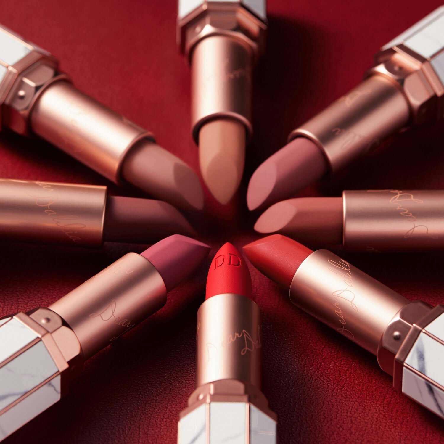 DEAR DAHLIA Lip Paradise Effortless Matte Lipstick in diverse shades arranged on a red background.