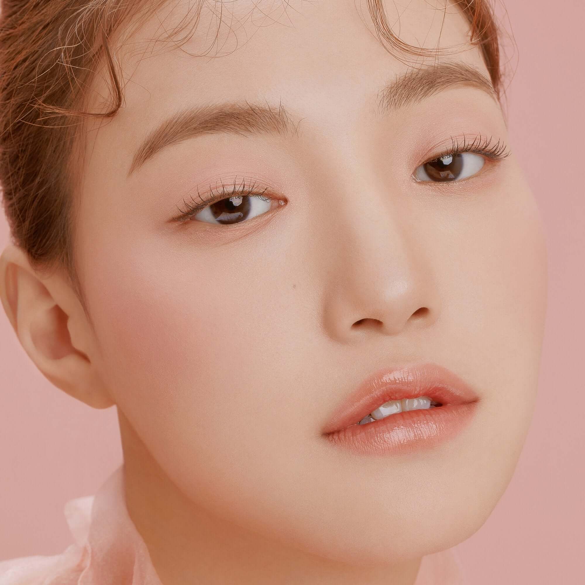 Close-up of a woman's face showcasing natural beauty, wearing DEAR DAHLIA Paradise Blooming Night makeup on a soft pink background.