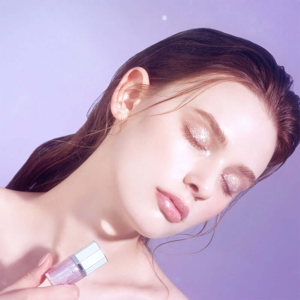Model with closed eyes showcasing DEAR DAHLIA Paradise Sparkle Lip Glaze on lips against pastel purple background.