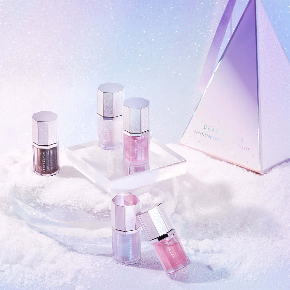 Assorted DEAR DAHLIA Paradise Sparkle Lip Glaze tubes displayed on a crystalline surface with pastel hues
