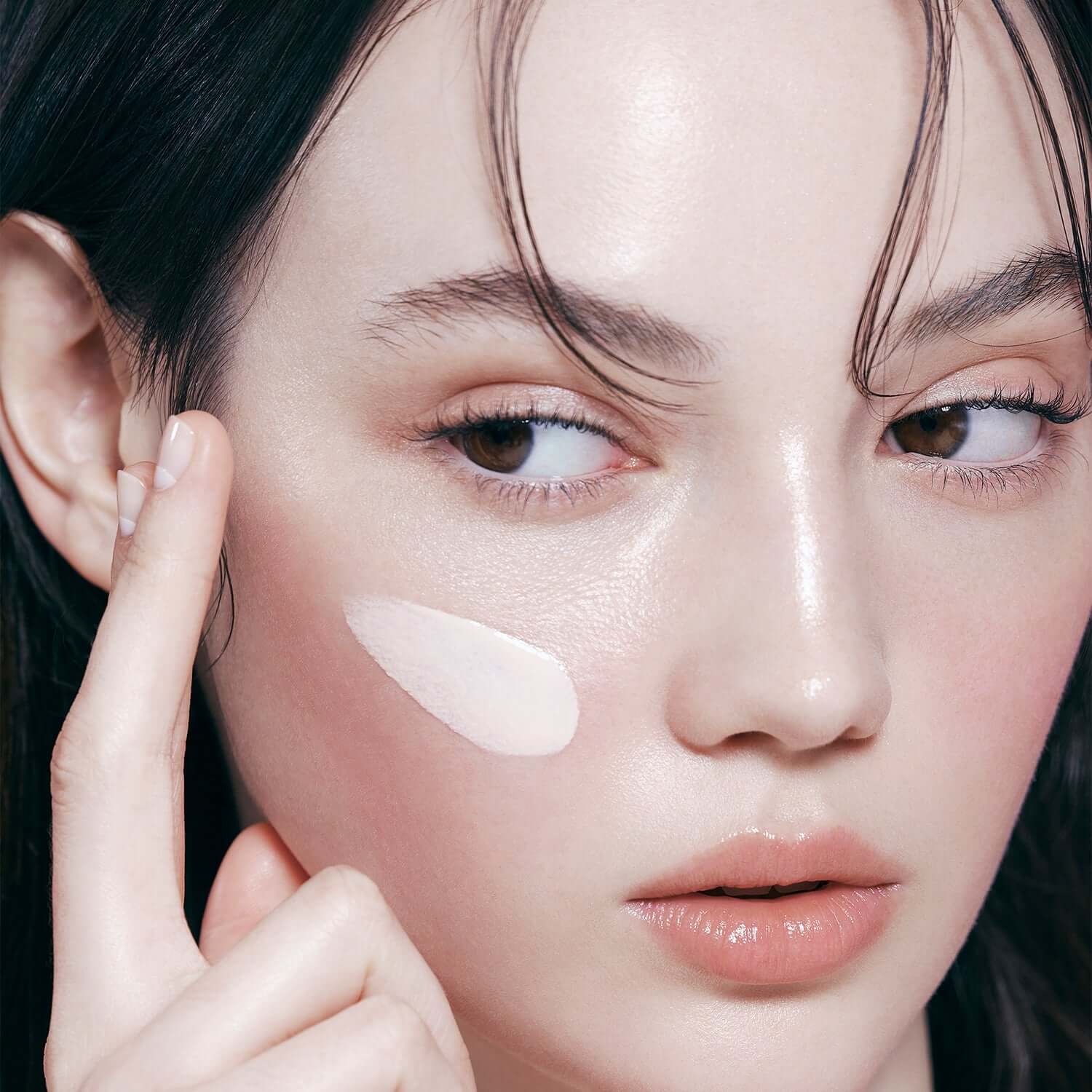 Model applying DEAR DAHLIA Prime Layer Glow Primer on cheek, showcasing its smooth texture and luminous finish for radiant skin.