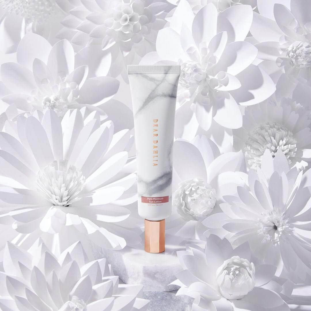 DEAR DAHLIA Skin Paradise Pure Moisture Sun Lotion surrounded by white flowers in a luxurious display