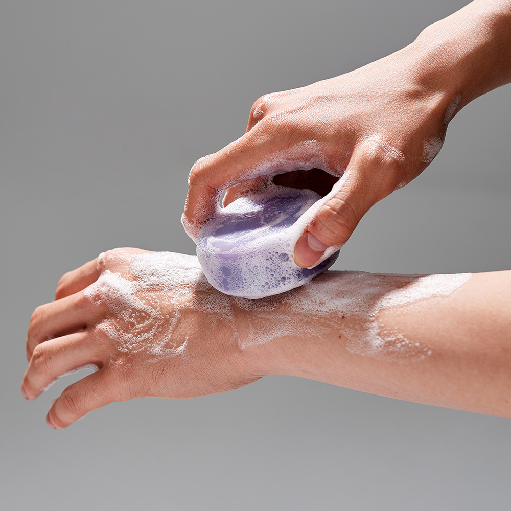 Person using DONGGUBAT Field Correct Cleansing Soap Collagen on arm, producing a lather with purple soap.